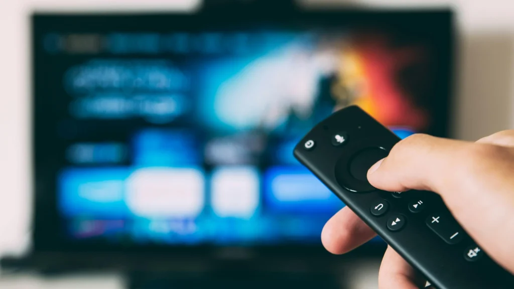 Hand holding a remote in front of a blurred IPTV interface.